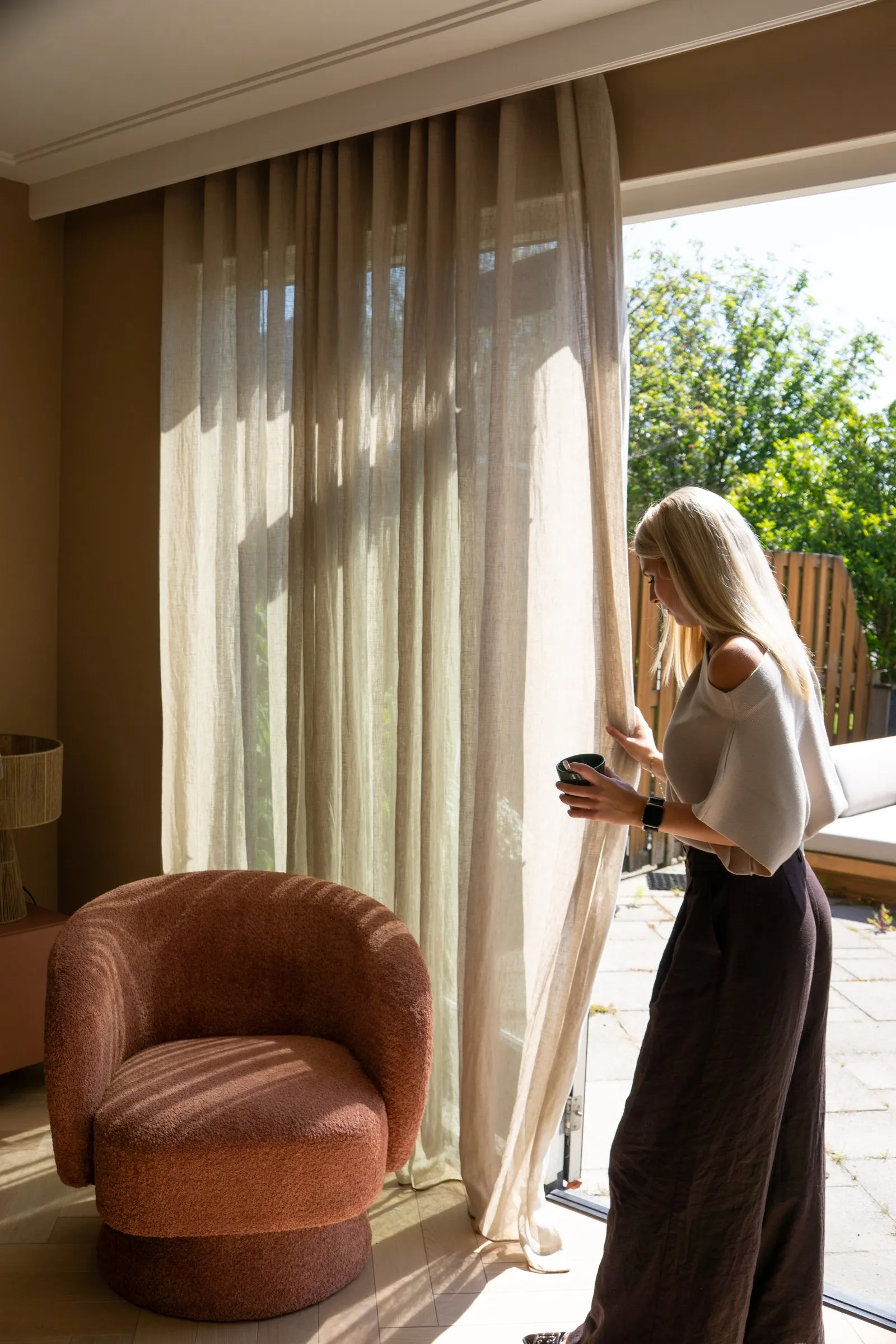 Vrouw bij het raam naast een terracotta fauteuil