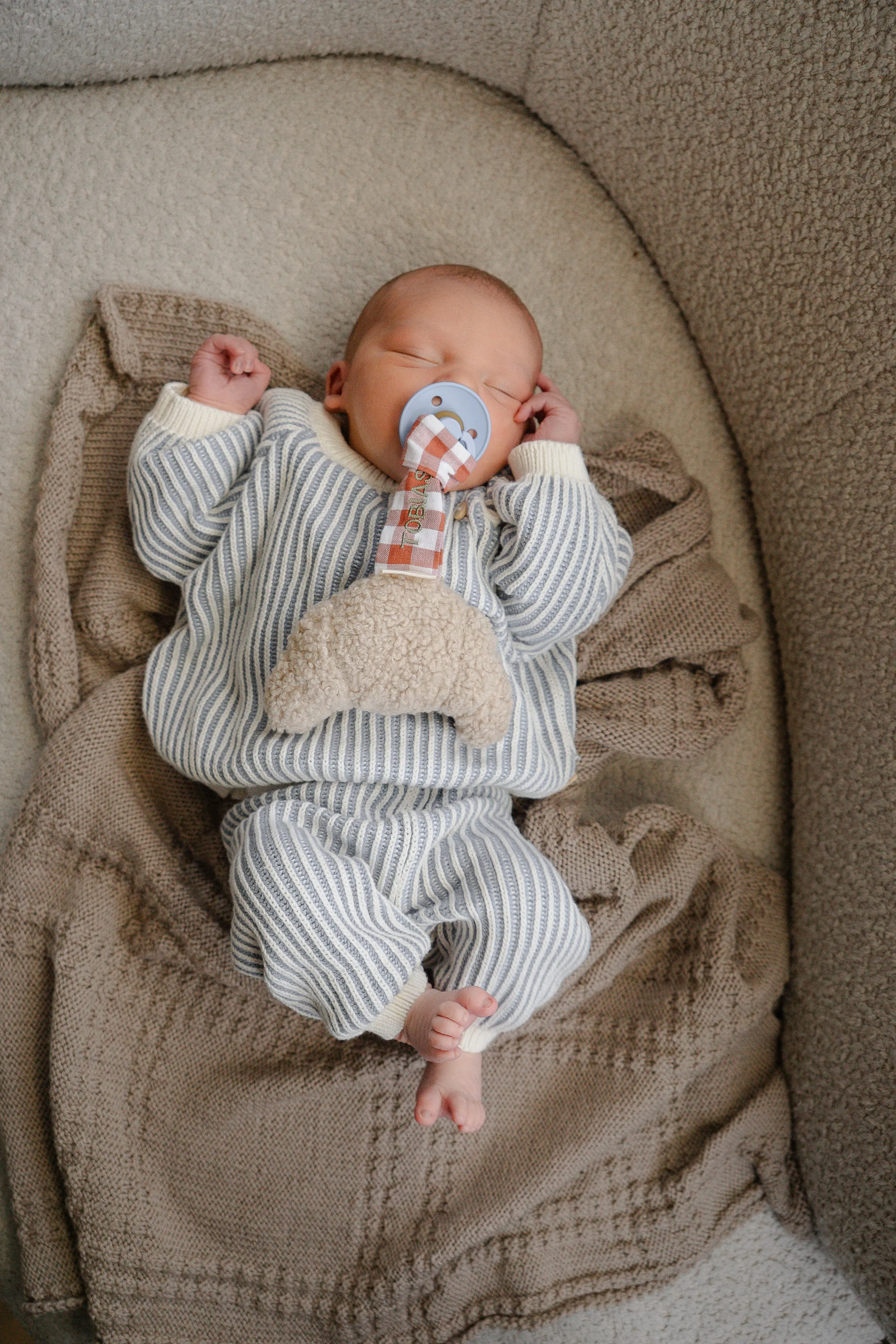 Baby met speen en schapenvachtje knuffel in gestreepte outfit